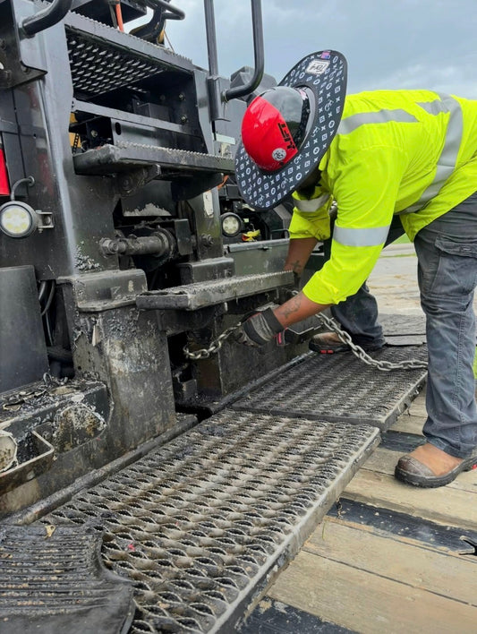 TG Black TEN4 sunshade worn on a red hard hat by a lineman handling a chain at a utility truck; original jobsite photo with modest lighting correction. Hard hat not included.