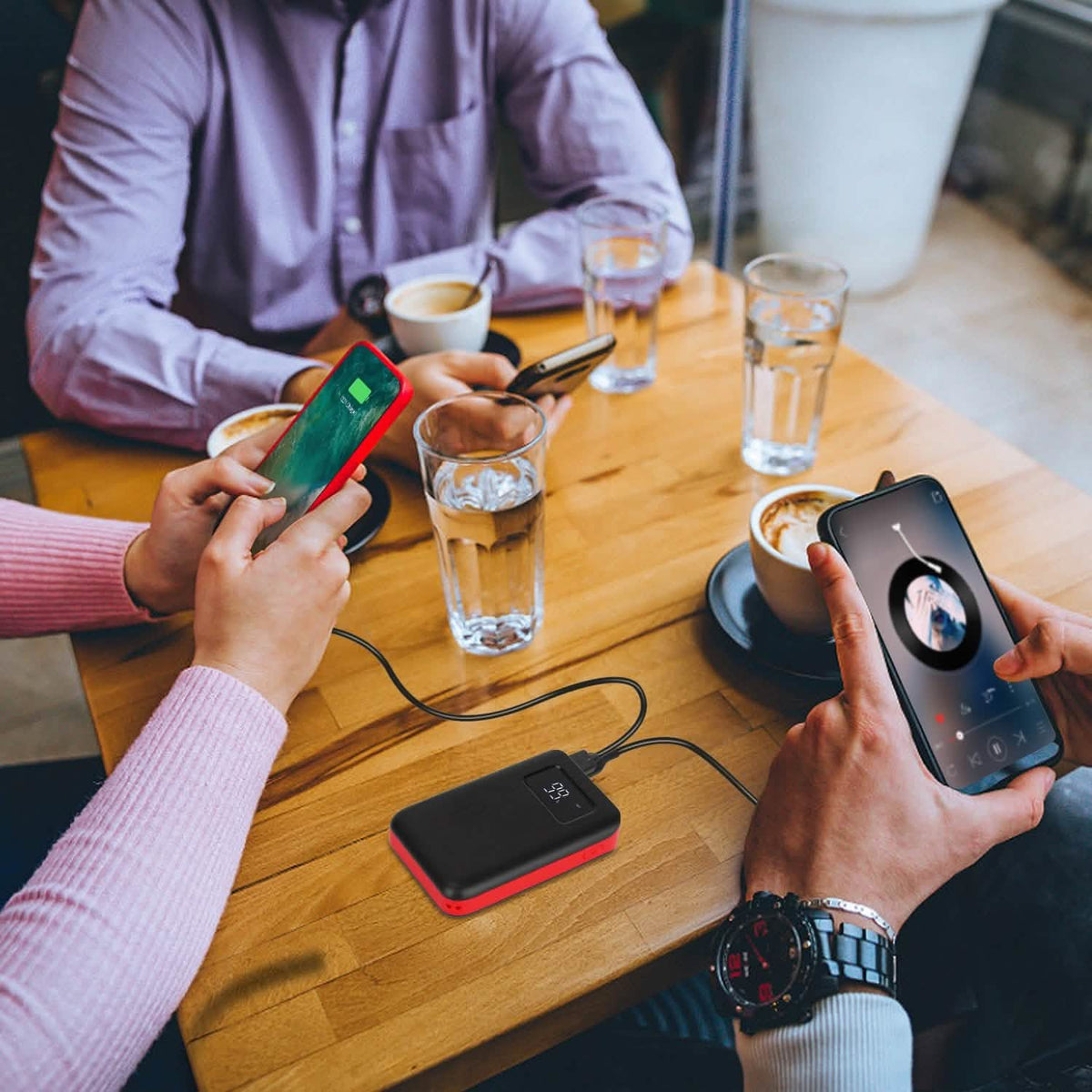 Portable power bank on a table beside people using smartphones