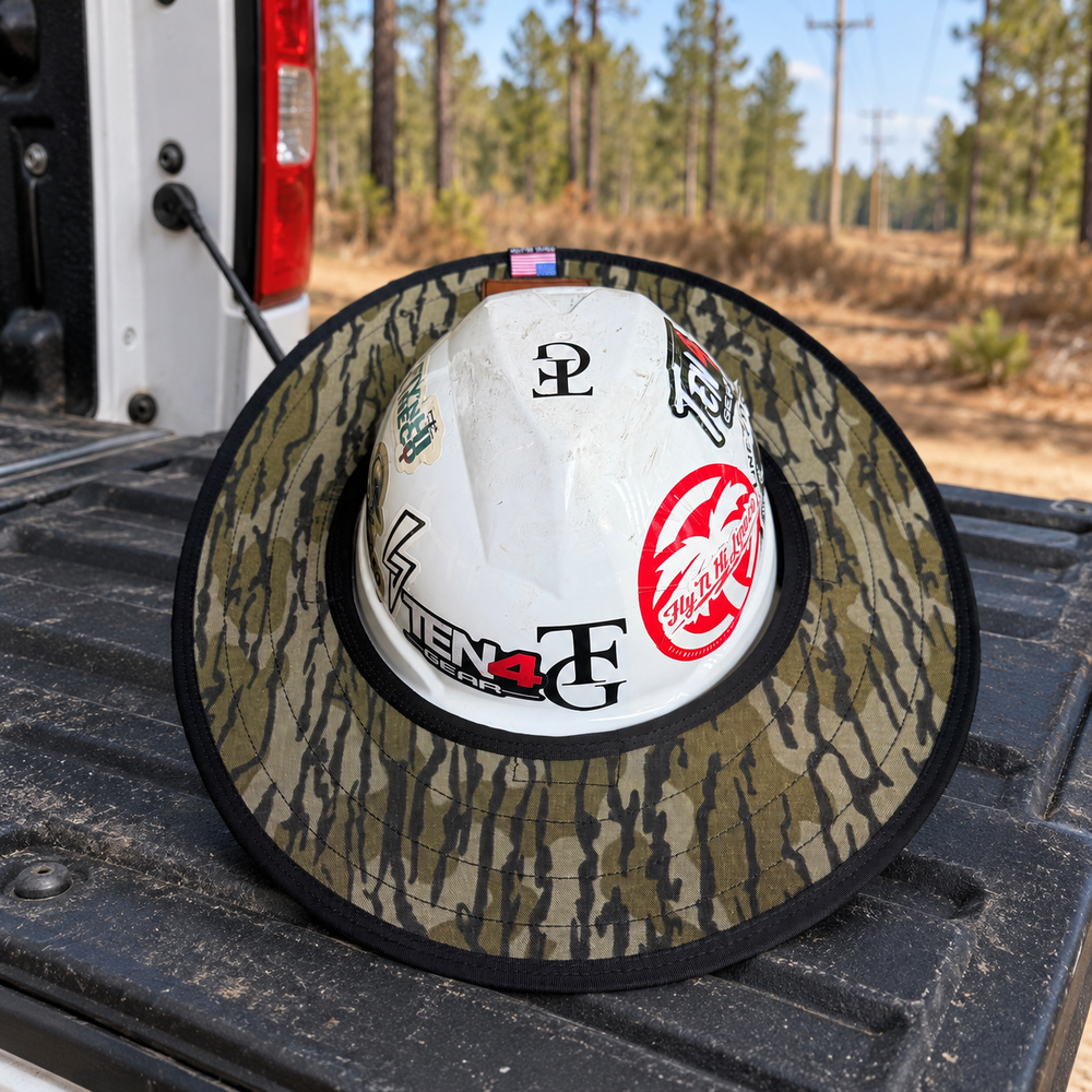 Bottomland camo sunshade mounted on a white hard hat on a truck tailgate at a woodland utility worksite