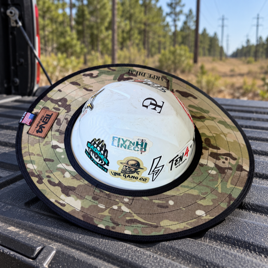 Defender camo sunshade on a white hard hat on a pickup tailgate at a wooded utility right of way