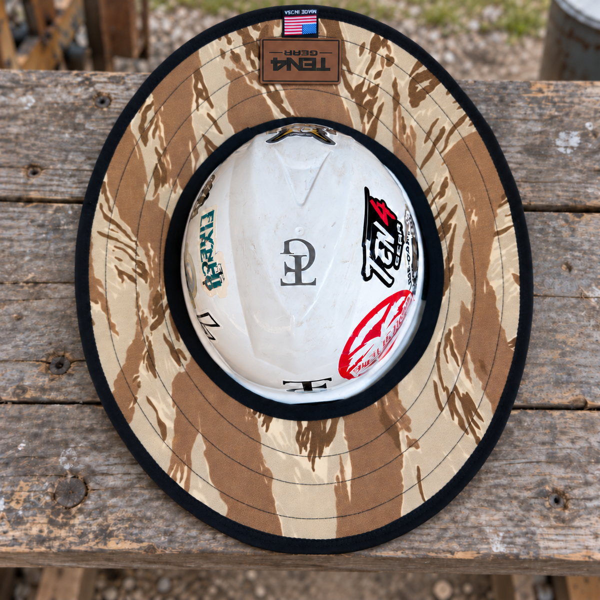 Desert Tiger Stripe sunshade on a hard hat with current TEN4 patch centered at the rear, on a rustic workbench