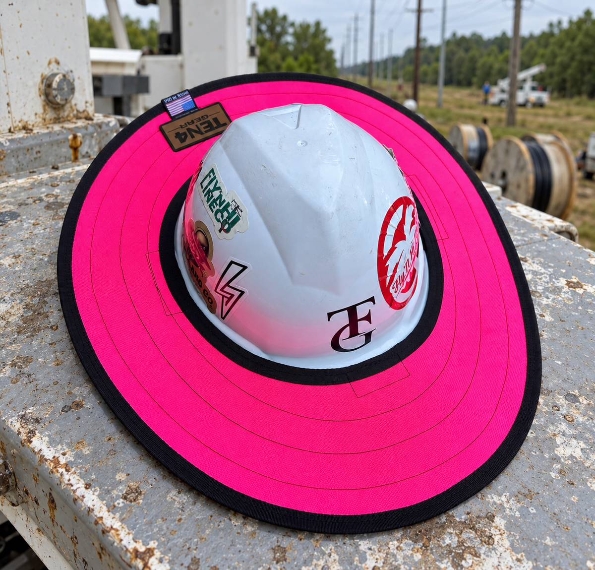 Electric Pink hard hat sunshade with current rear TEN4 patch on a utility truck at a linework site