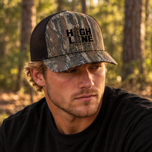 Young blond model in a black shirt wearing the TEN4 HIGH LINE woods camo trucker hat in the woods