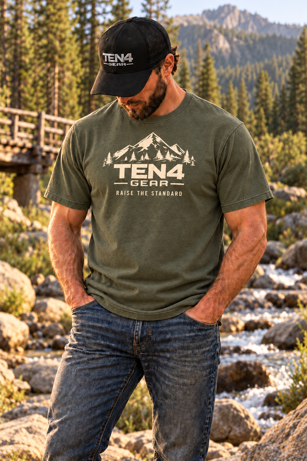 TEN4 Raise the Standard tee in Moss, cream mountain design on model beside a wooded creek