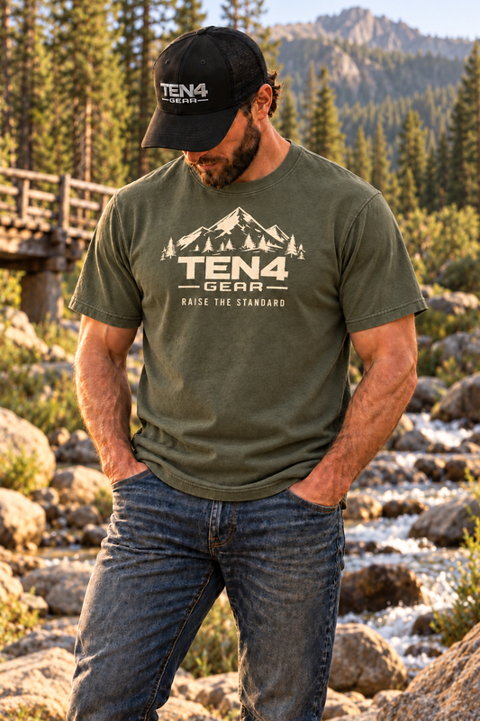 TEN4 Raise the Standard tee in Moss, cream mountain design on model beside a wooded creek