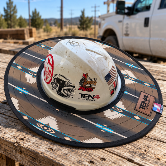 RanchHand sunshade in tan, charcoal, cream and turquoise on a white hard hat, resting on a weathered wood table beside a work truck