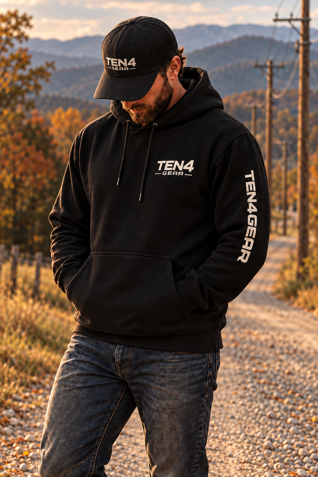 TEN4 Sleeve Hit black hoodie with cream chest and left sleeve logos, on our bearded model beside wooden utility poles and Blue Ridge mountains.