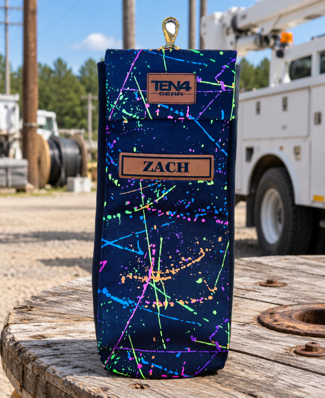 Splatter Classic bag with flat Velcro flap and personalized leather name patch — original product photo; background edited to an outdoor utility jobsite.